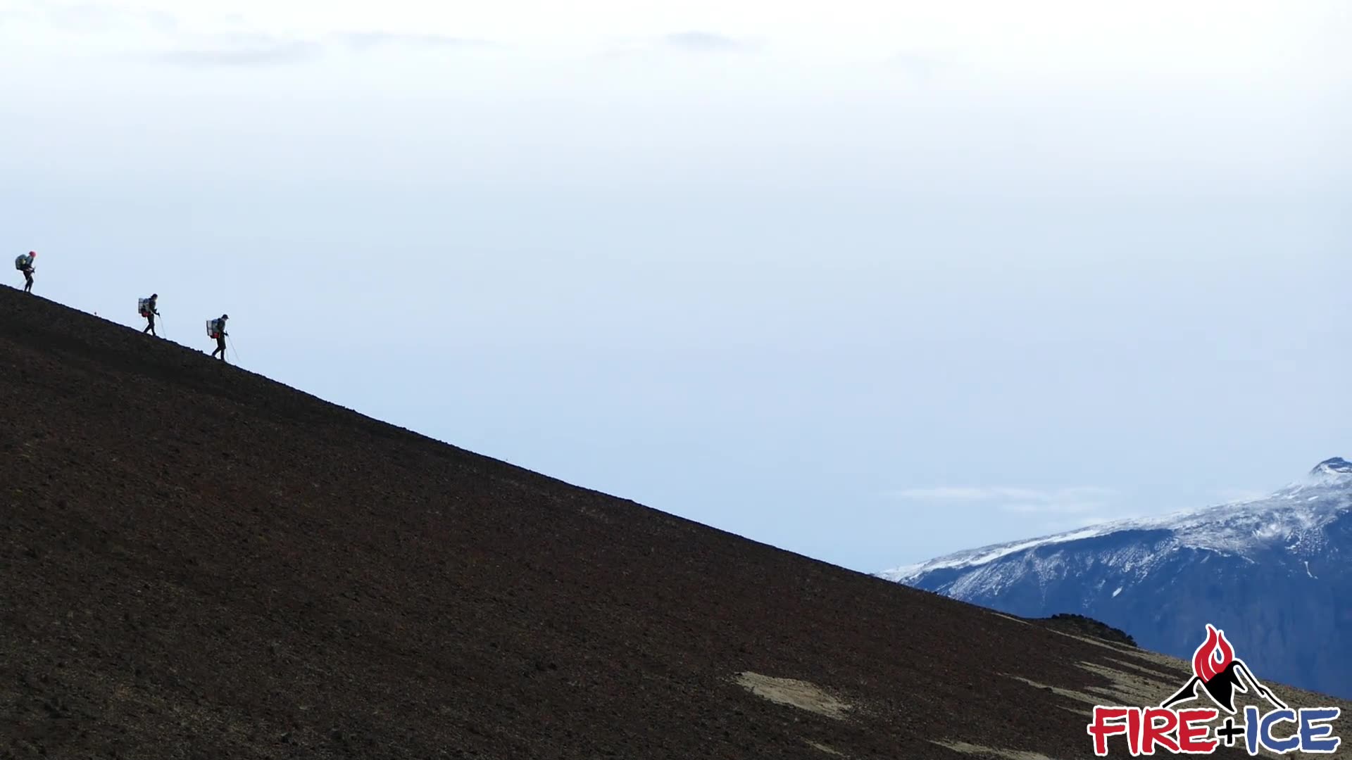 Competitors climbing a black volcanic ridge in the Icelandic interior, snow-capped mountains beyond